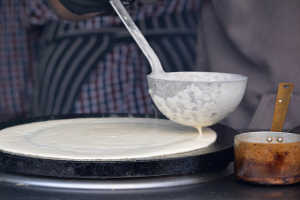 Use a ladle to evenly spread the pancake batter across the pan.